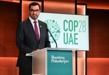 COP in crisis Sultan Al Jaber stands at a podium, speaking, with a COP28 sign behind him on stage
