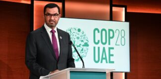 COP in crisis Sultan Al Jaber stands at a podium, speaking, with a COP28 sign behind him on stage