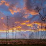 Market-wide Half-Hourly Settlement: Fundamental change to the UK electricity market A row of electricity pylons in front of a setting sun, potentially to be impacted by Market-wide Half-hourly settlements