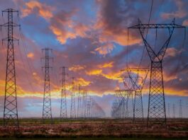 Market-wide Half-Hourly Settlement: Fundamental change to the UK electricity market A row of electricity pylons in front of a setting sun, potentially to be impacted by Market-wide Half-hourly settlements