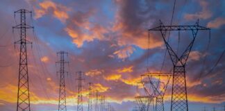 Market-wide Half-Hourly Settlement: Fundamental change to the UK electricity market A row of electricity pylons in front of a setting sun, potentially to be impacted by Market-wide Half-hourly settlements