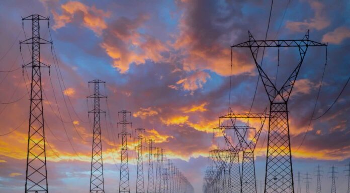 Market-wide Half-Hourly Settlement: Fundamental change to the UK electricity market A row of electricity pylons in front of a setting sun, potentially to be impacted by Market-wide Half-hourly settlements