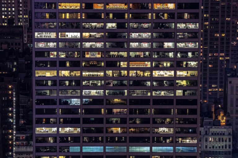 An office building is lit up at night, showing the empty rooms inside.