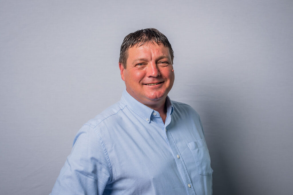 A headshot of Aidan Lupton - a middle-aged white male with short brown hair. Aidan is wearing a light blue button-up shirt.