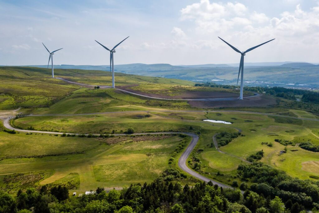 Wind turbines on the horizon stand above green hills in Wales