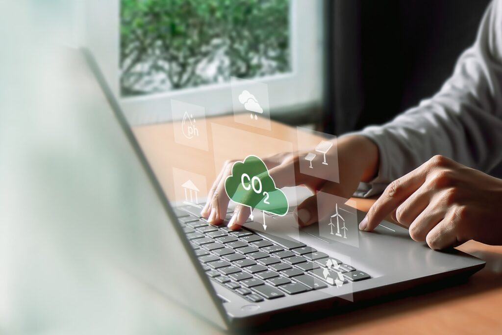 A man types on his computer, working on an ESG report. Symbols hover above his keyboard in a futuristic way, including symbols such as windmills and a CO2 cloud.