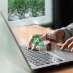 Understanding ESG: Environmental, Social, and Governance A man types on his computer, working on an ESG report. Symbols hover above his keyboard in a futuristic way, including symbols such as windmills and a CO2 cloud.