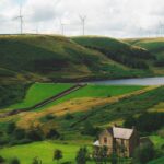Latest CfD round enough to power 11 million UK homes View of the Greenbooth Reservoir, Greater Manchester, England. A stone house sits by the reservoir with wind turbines on the ridge in the distance.
