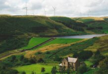 Latest CfD round enough to power 11 million UK homes View of the Greenbooth Reservoir, Greater Manchester, England. A stone house sits by the reservoir with wind turbines on the ridge in the distance.
