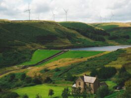 Latest CfD round enough to power 11 million UK homes View of the Greenbooth Reservoir, Greater Manchester, England. A stone house sits by the reservoir with wind turbines on the ridge in the distance.
