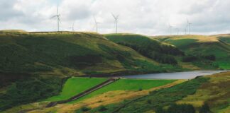 Latest CfD round enough to power 11 million UK homes View of the Greenbooth Reservoir, Greater Manchester, England. A stone house sits by the reservoir with wind turbines on the ridge in the distance.