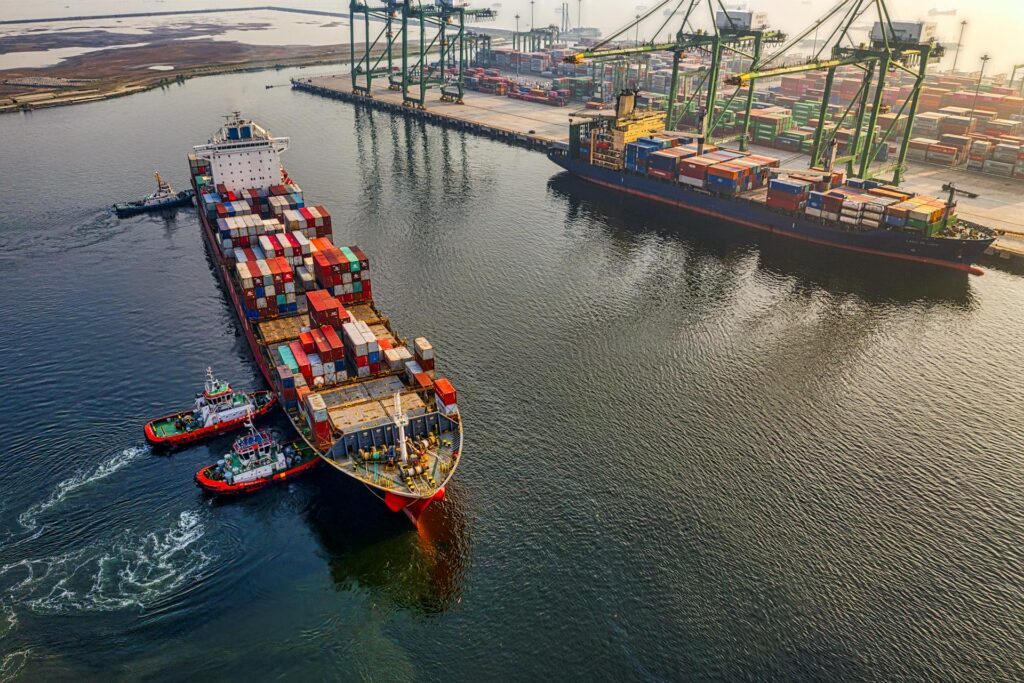 Three small tugboats guide a large cargo ship to the dock