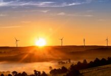 Government unveils Clean Power Action Plan to achieve 2030 energy goals The sun sets on the horizon, outlining wind turbines on the crest of a hill