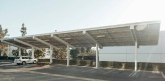 Government considers mandating solar PV in car parks A white car sits under a solar carport on a sunny day.