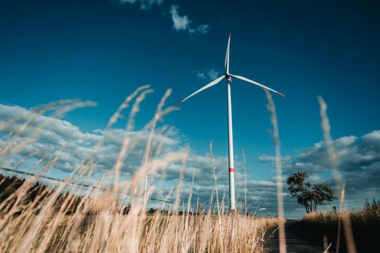 A wind turbine on a field with blue sky behind it.