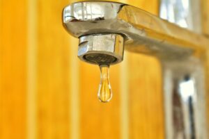 water drips from a tap faucet with a bright yellow wall behind it