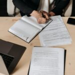 Consultation: government seeks views on UK Sustainability Reporting Standards Professional person writing in a journal on a desk. A laptop and other shets of paper are also on the desk.