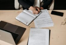 Consultation: government seeks views on UK Sustainability Reporting Standards Professional person writing in a journal on a desk. A laptop and other shets of paper are also on the desk.