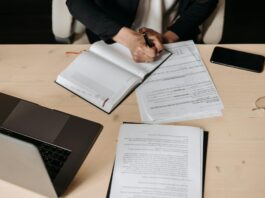 Consultation: government seeks views on UK Sustainability Reporting Standards Professional person writing in a journal on a desk. A laptop and other shets of paper are also on the desk.